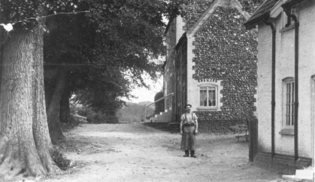 Historical black and white photograph of London Lane in Mundford with a man standing in the road and a flint cottage to the right